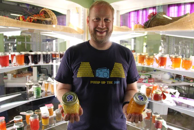 Ben Chapman holding a jam and a jelly in front of glass display cases at the N.C. State Fair. 