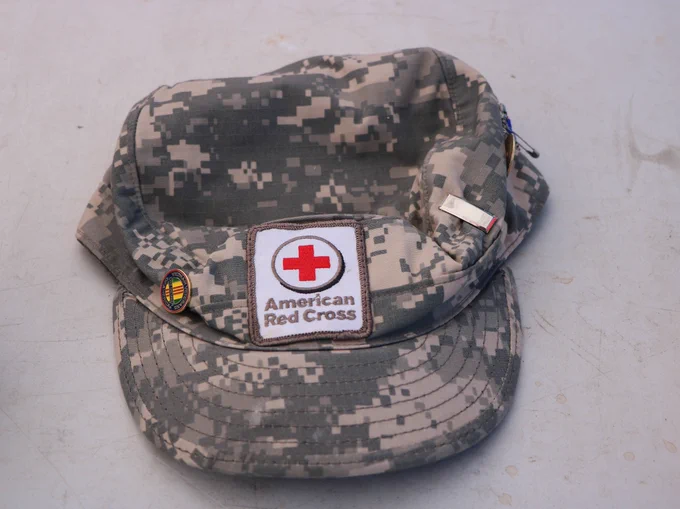 A camouflage-patterned cap with a prominent American Red Cross patch on the front.