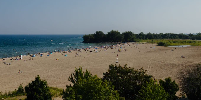 Wide sandy beach with scattered sunbathers and swimmers near calm blue water under a clear sky.