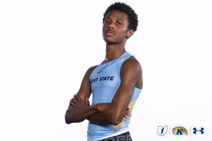 A person is posing confidently with arms crossed, wearing a light blue athletic top with "Kent State" written on it. The logos for Kent State University, Under Armour, and a silhouette of a state are at the bottom right.