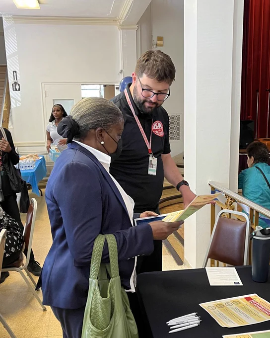OIG staffer in a black shirt sharing literature with a member of the community in blue and white.