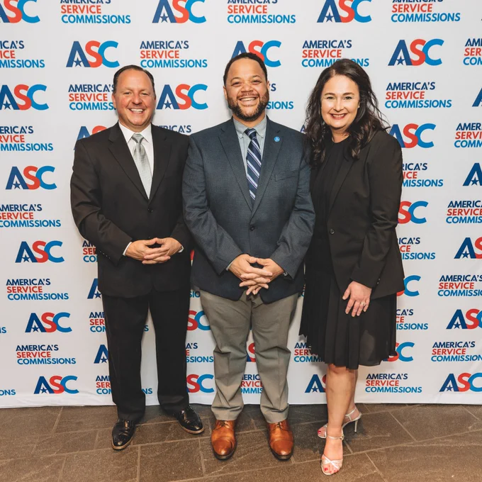 Three people stand in front of a background with the ASC logo.