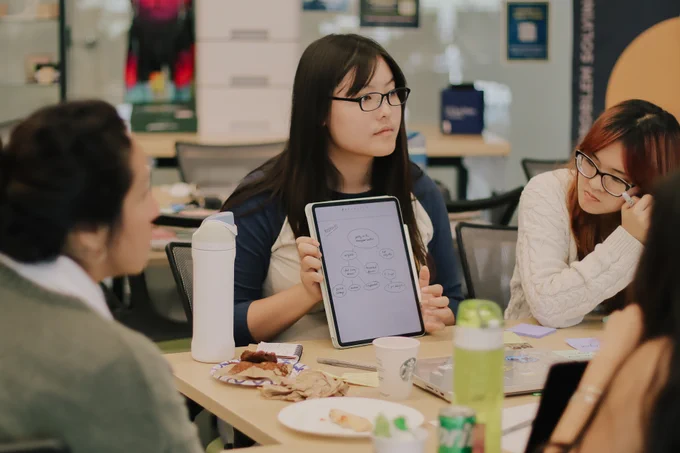 Person holding diagram with iPad and other people watching