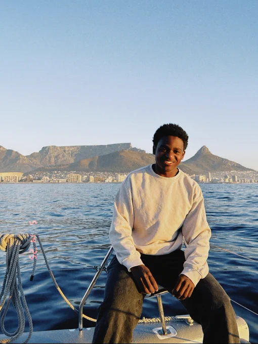 A person sits on a boat with a view of Table Mountain and the Cape Town cityscape in the background. The ocean is calm under a clear blue sky.
