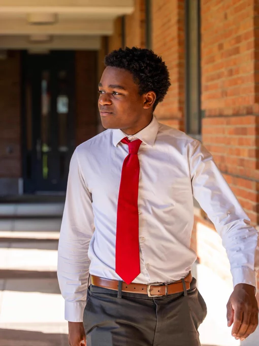 Student in white shirt and red tie walking through a brick courtyard.