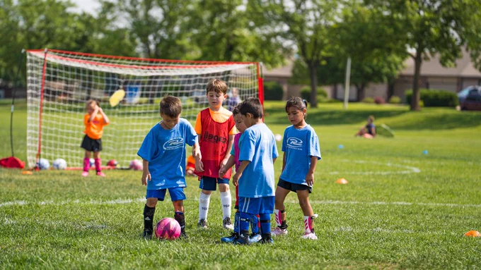 Young athletes play soccer in the park during summer camp.
