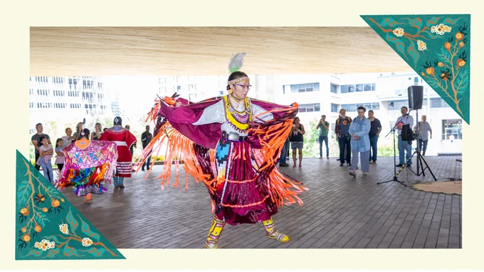 A person performing an Indigenous dance in a spacious outdoor setting in front of an audience. The scene is framed with Indigenous artwork.