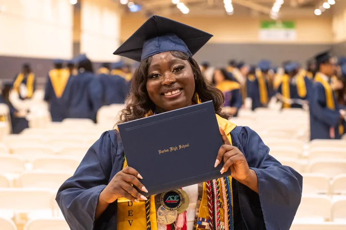 A smiling woman in graduation cap and gown holding a diploma at a graduation ceremony.