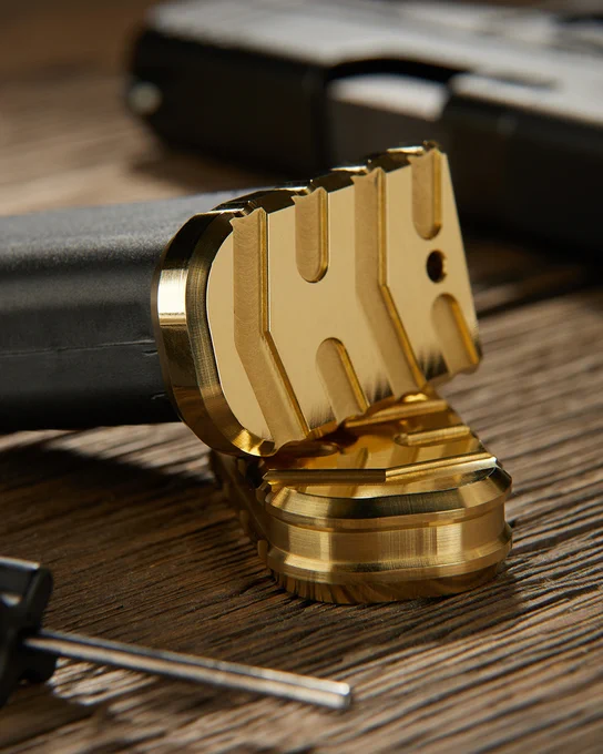 Close-up view of a magazine equipped with a precision-machined brass magazine base plate. An additional brass plate stands upright nearby, highlighting the detailed milling and metallic finish.