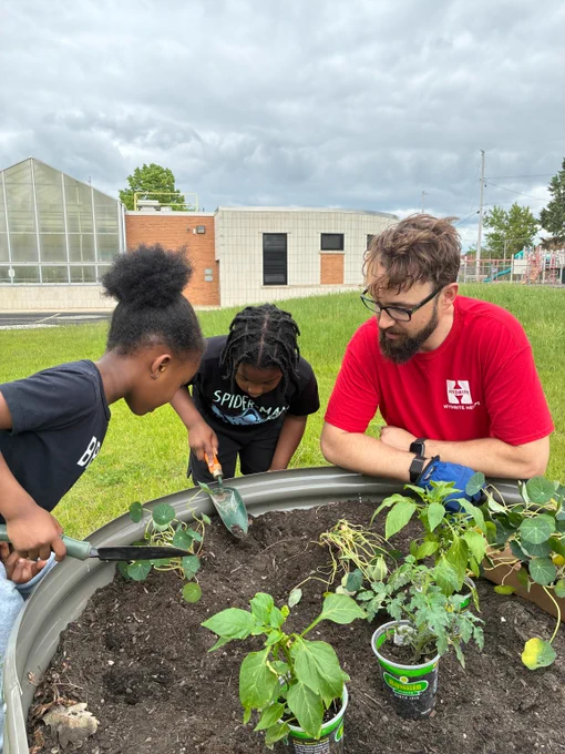 A Hydrite Helps volunteer gives instructions to kids digging holes for plants in a raised garden bed.