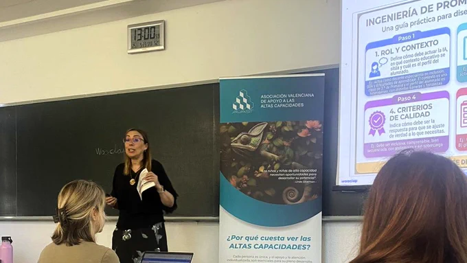 Fotografía de Concha Barceló dando una charla para AVAST. Está de pie en un aula, con un enrollable corporativo de la asociación a su lado que dice "¿Por qué cuesta ver las Altas Capacidades?". A la derecha, parte de la pantalla de proyección muestra una diapositiva titulada "INGENIERÍA DE PROMPTS." con pasos prácticos sobre cómo usar la IA (como "1. Rol y contexto" y "4. Criterios de calidad"). Barceló, con gafas y camisa negra, sostiene un papel mientras habla