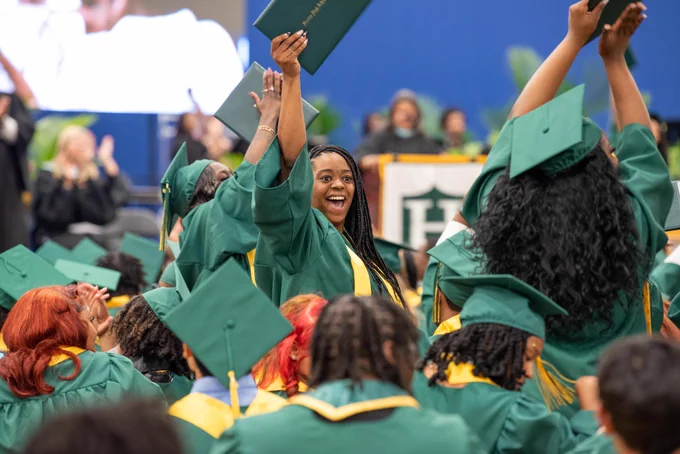 A group of graduates dressed in green graduation gowns and caps celebrating their achievement.