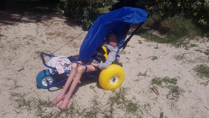 Im Strandrollstuhl mit Sonnenschirm am Sandstrand.