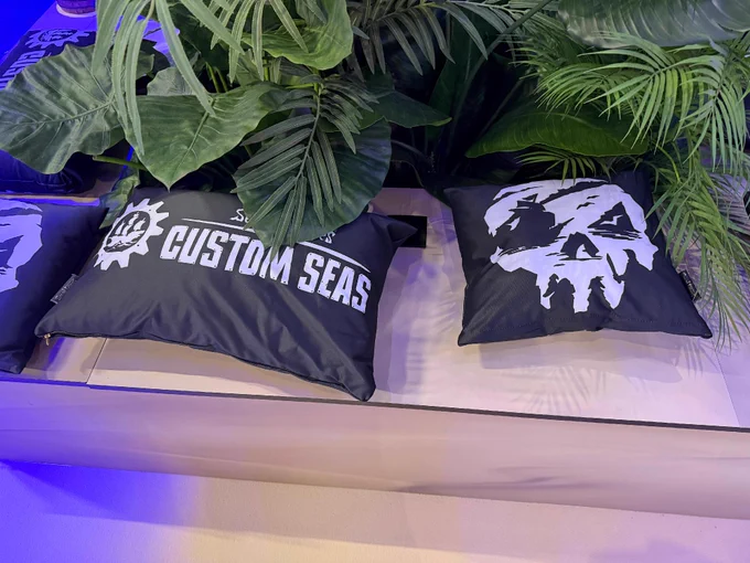 A photograph of the Sea of Thieves stand at TwitchCon Europe showing some cushions on a bench. One features the Sea of Thieves logo, the other says "Sea of Thieves Custom Seas".