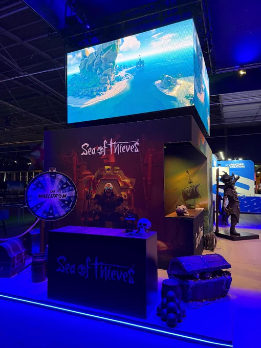 A photograph of the Sea of Thieves stand at TwitchCon Europe, complete with a big screen running a trailer and a wheel to spin for fun behind a counter.