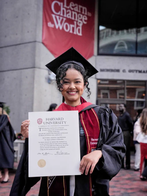 Mutiara Baswedan tersenyum mengenakan toga hitam, mortarboard, dan selempang merah Harvard University sambil menunjukkan ijazah Master of Education ke arah kamera. Tia berdiri di depan gedung Monroe C. Gutman Library, Harvard Graduate School of Education, dengan spanduk merah bertuliskan “Learn to Change the World” terlihat di latar belakang.