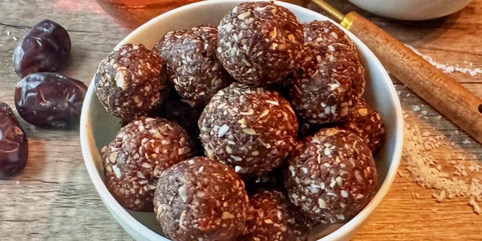 Bowl filled with homemade chocolate energy balls made from oats and dates on a wooden table.