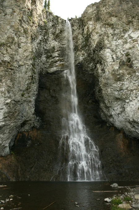 A tall, thin waterfall into a small pond surrounded by rocky cliffs