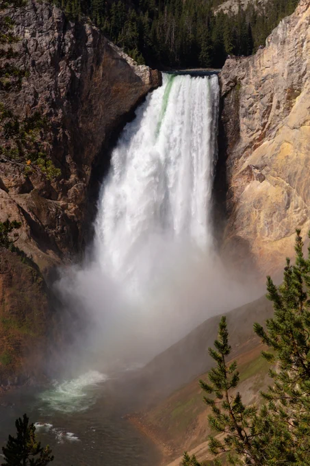 A large, tall waterfall plunging into a river below surrounded by golden-colored rocky cliffs.