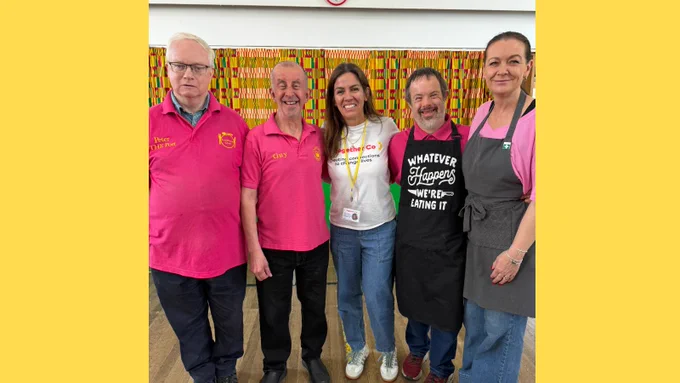 Our social prescribing link worker, Vanina, is stood in the middle of four people who help out at the Food and Friendship lunch. They have their arms around each other's backs and are smiling at the camera