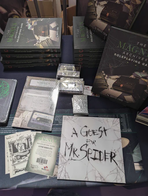 A photograph of The Magnus Archives Roleplaying Game, and some associated merchandise available at the Monte Cook stand. 