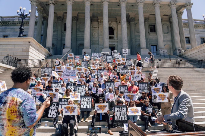 Rally on the Statehouse steps. Signs say "It's about us," "Black voters matter," and "This is what democracy looks like"