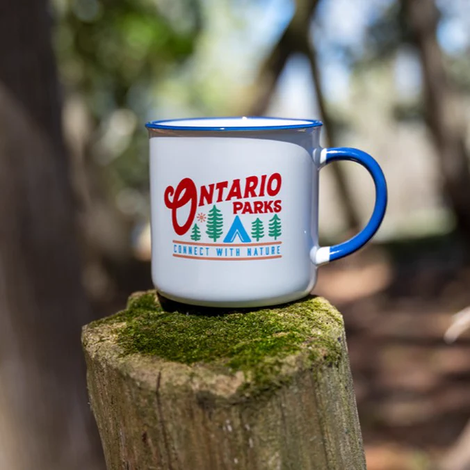 White mug with a colourful Ontario Parks logo resting on a wooden post.