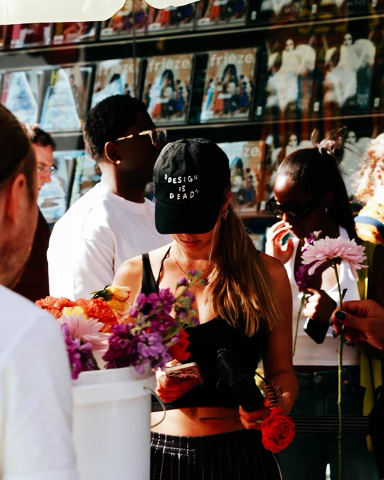 Person wearing a "Design is dead" hat, in front of flowers