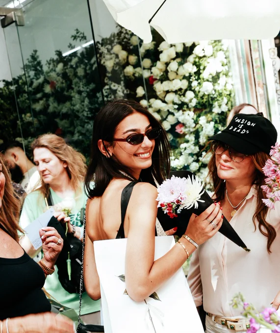 People in front of flowers, with one person wearing a "design is dead" hat.
