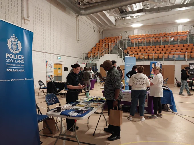 Police Scotland stall at an indoor event with leaflets and a police officer. Other stalls and people are visible.