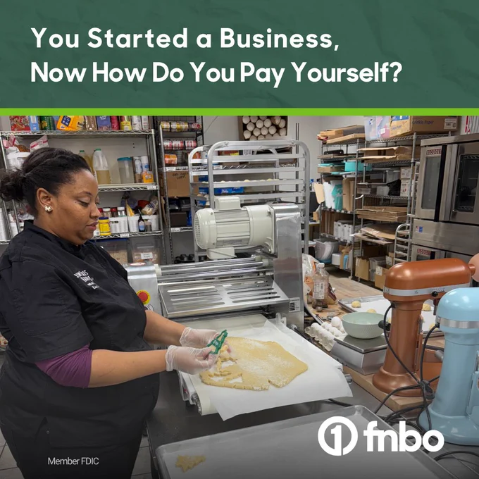 A person working in a bakery is cutting dough on a table. There are appliances and supplies in the background. Text reads, “You Started a Business, Now How Do You Pay Yourself?” The logo for FNBO is in the bottom right corner.