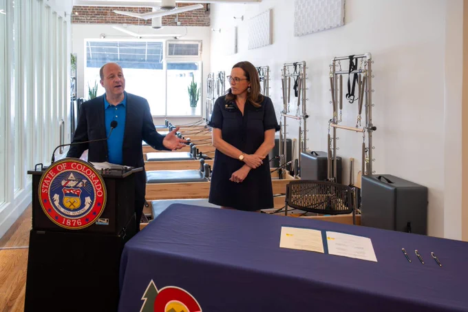 Governor Jared Polis is giving remarks for a bill signing in a pilates studio.