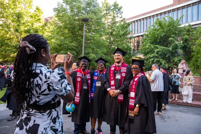 Four graduates smiling and posing while a family member takes their photo.
