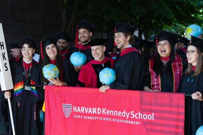 A group of graduates smiling for a photo with Dean Jeremy Weinstein and holding a Harvard Kennedy School banner.