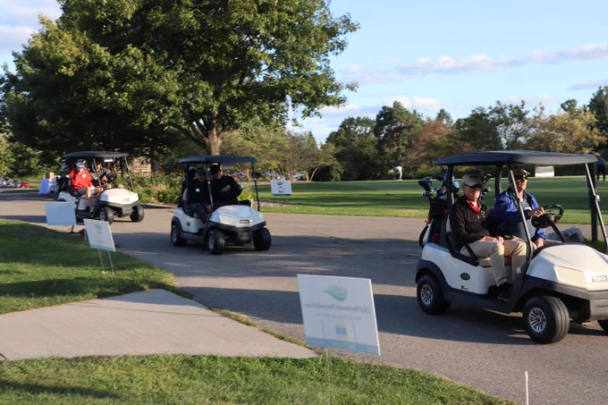 Golf carts taking off single file down a paved path towards the golf course at last year's Shot in the Dark.