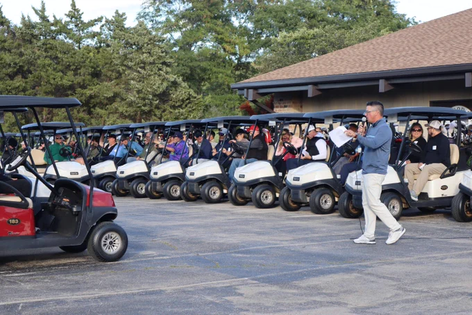 Golf carts lined up and preparing to take off as a staff member directs them.
