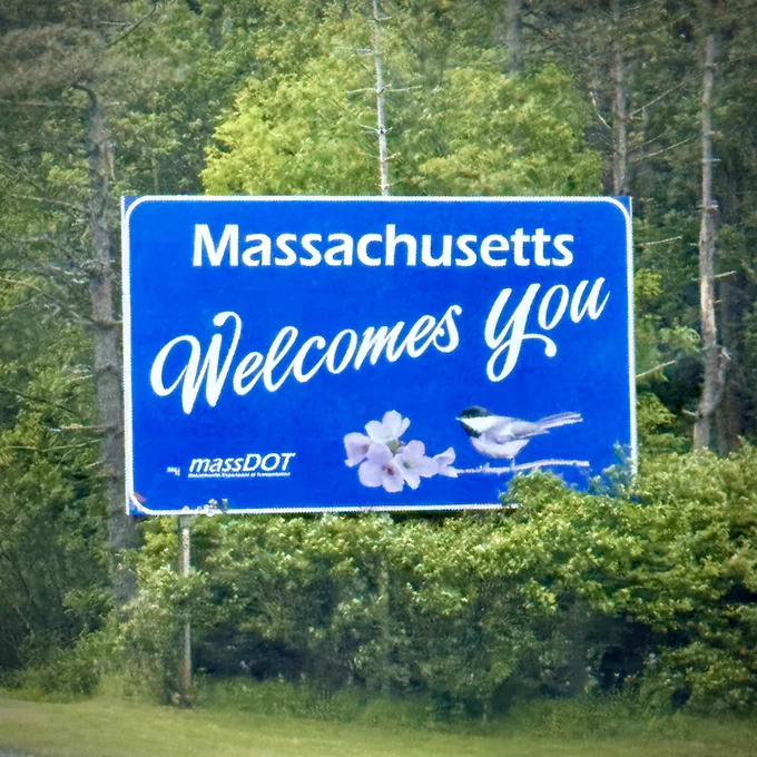 A large blue sign on the side of the thruway that said “Massachusetts Welcomes You”