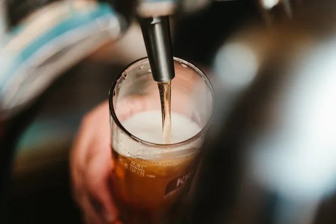 View from above of a pint of beer being poured into a glass from a tap