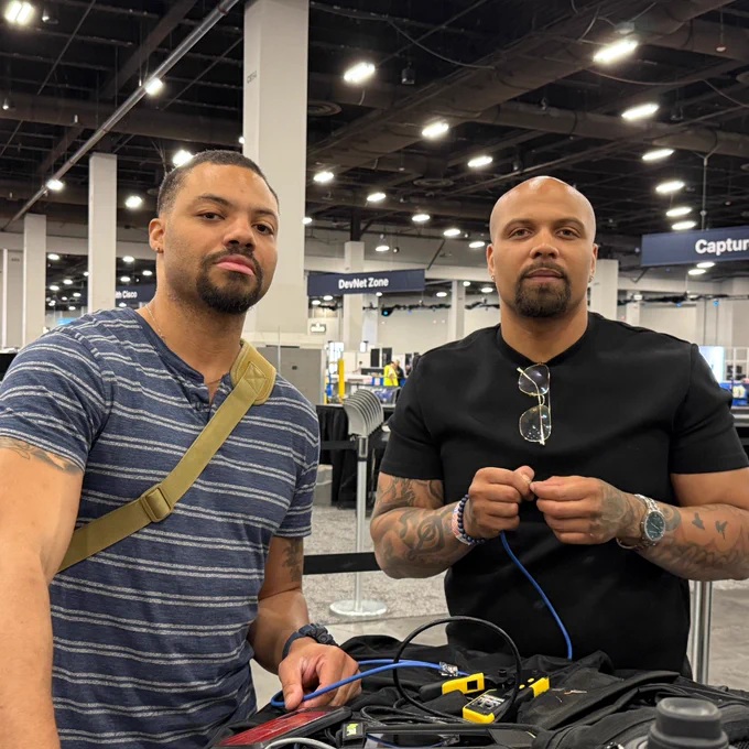 Two men in an event space, one holding a network cable and crimping tools.