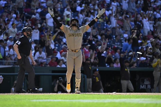 Fernando Tatis Jr. pointing up to the sky in celebration after hitting a home run. He is wearing the Padres tan pinstripe uniform.