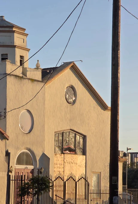 The exterior of a church with a partially boarded up stained glass window. One pane of the window is broken and red duct tape covers the broken edges