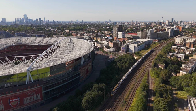 Aerial view of Arsenal’s stadium beside railway tracks, with London’s skyline in the background