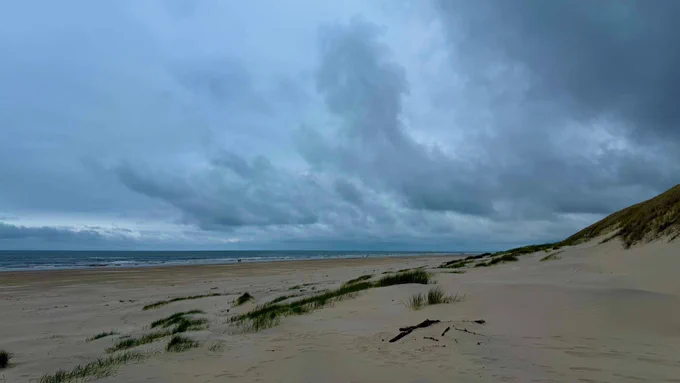 Am Strand: links das Meer, rechts die Dünen. Stark bewölkter Himmel mit dramatischer Wollenstimmung.