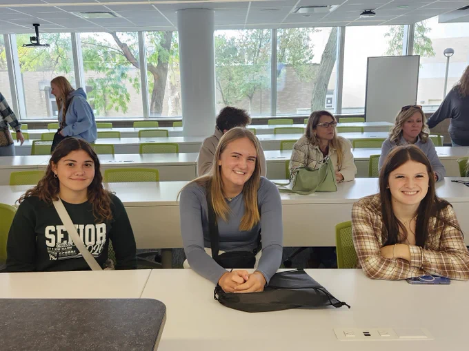 Three students sit at a desk and smile during Wayne State University College of Nursing tour