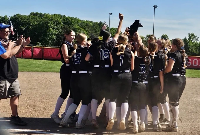 girls varsity softball holding the district trophy in the air