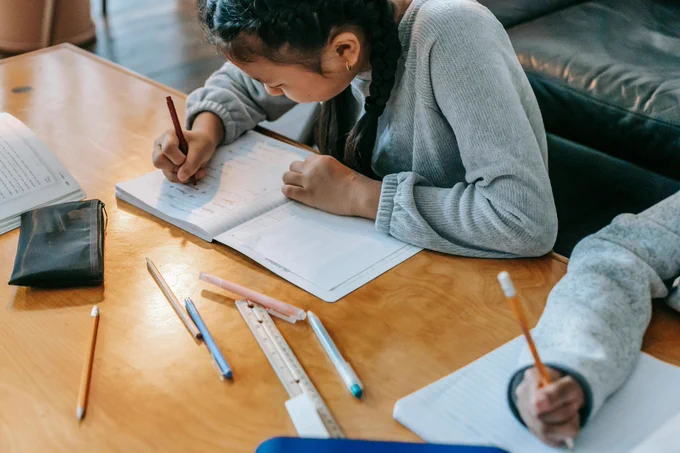 A young student sits at a table writing notes in a notebook.