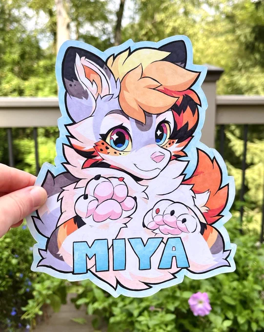 A fursona badge created using traditional materials such as brush ink pens and alcohol makers. It features a koi-fish fox character named “Miya”. She has her paws in the air, and her fluffy tail is placed behind her.