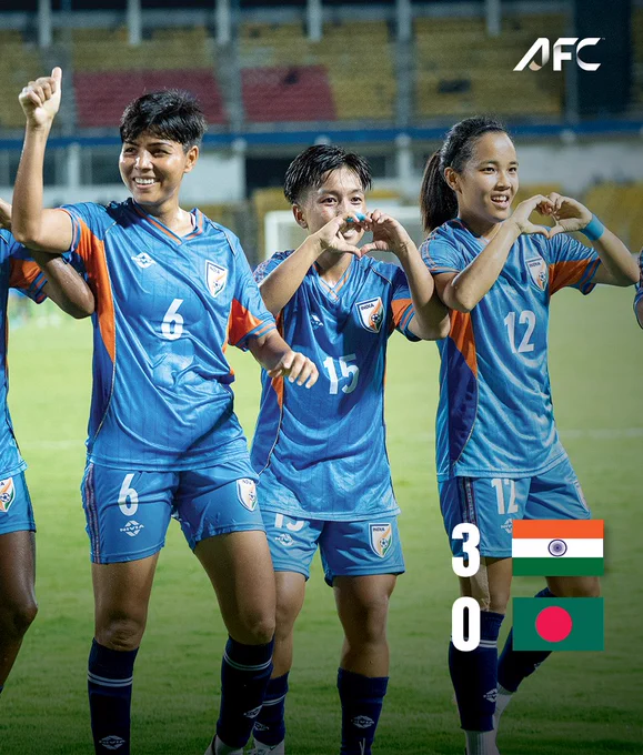 Indian women's football team players celebrate their 3-0 victory against Bangladesh. The players are smiling and making heart symbols with their hands, showcasing a sense of achievement and joy.