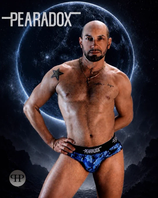 Shirtless model posing in blue camouflage Pearadox briefs against a glowing cosmic blue moon and star-filled night sky. 
