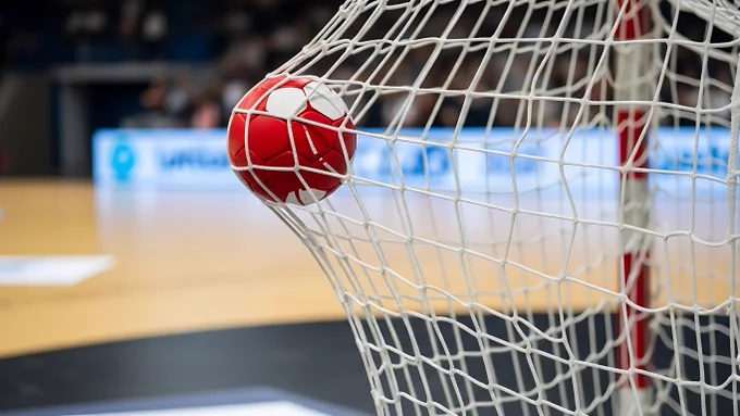 Ein roter Handball befindet sich in einem Tornetzkäfig auf einem Handballfeld.